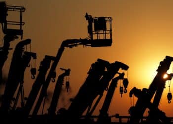 Cranes and boom lifts stand at an equipment rental company near a construction site in Japan.
