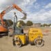 A builder drives a Terex Corp. ride-on roller past an excavator during house construction at Persimmon Plc's St. Andrew's Park residential housing development in the Uxbridge district of London, U.K., on Monday, Aug. 18, 2014. Persimmon, the U.K.'s largest homebuilder by market value, said sales of houses and apartments rose 28 percent in the first half as demand from buyers increased.