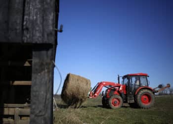 A farmer operates a tractor to transport a bale of hay at a farm in Pleasureville, Kentucky.