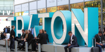 Attendees sit beside a Traton logo outside the Volkswagen AG (VW) exhibition area at the IAA Commercial Vehicles Show in Hanover, Germany, on Wednesday, Sept. 19, 2018. Volkswagen AG's truck unit is pushing to reduce its dependence on its main European market and lift profit margins in a challenge to commercial-vehicle industry leaders Daimler AG and Volvo AB.